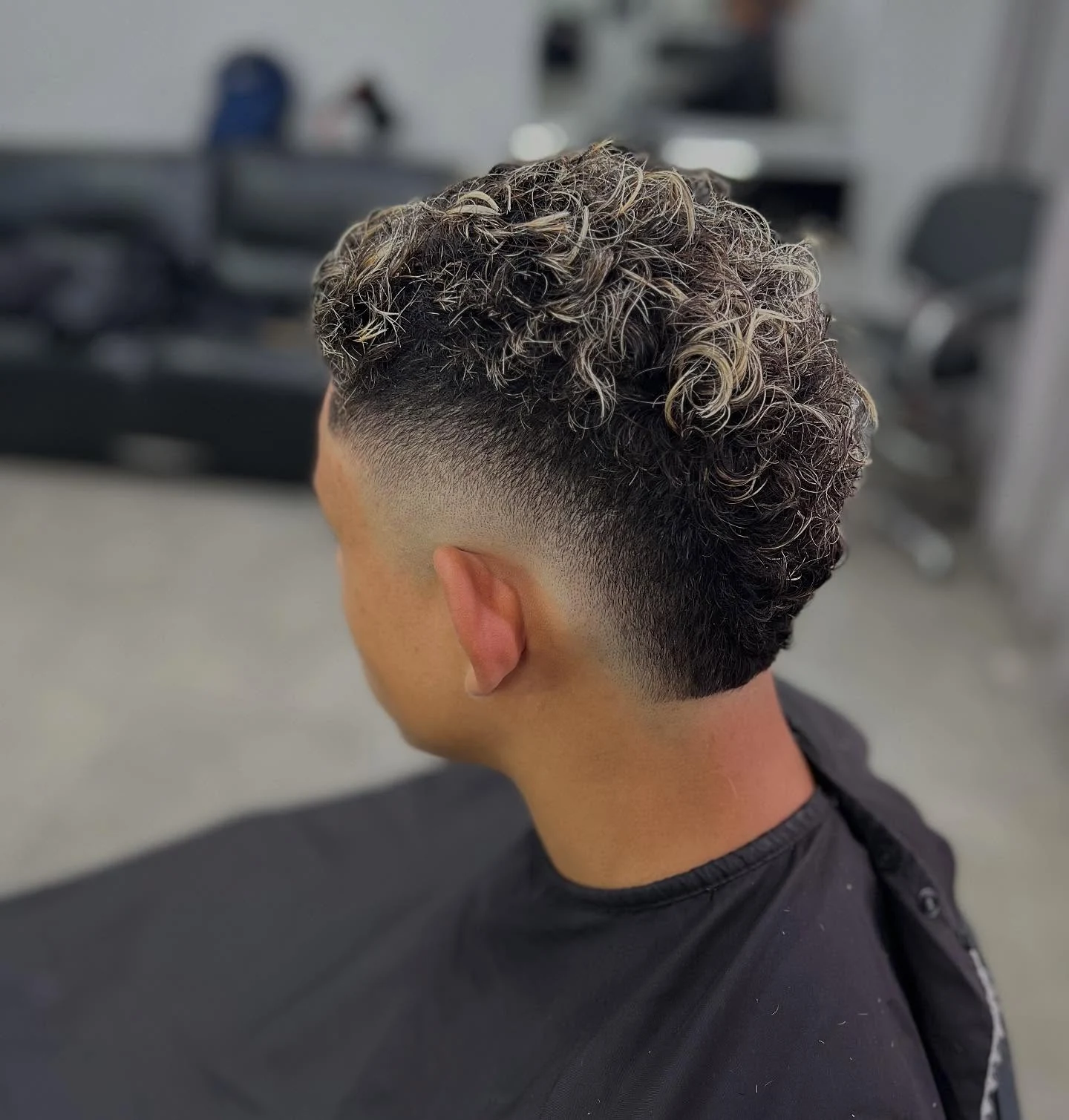 Corte cacheado com mechas claras e laterais curtas